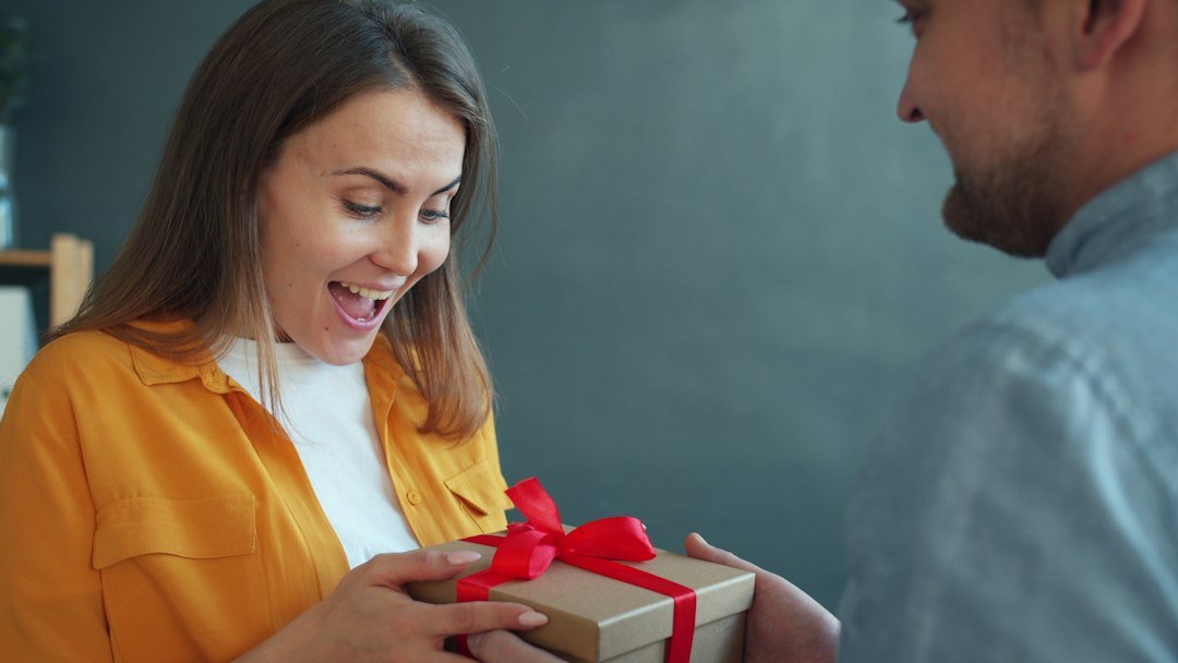 Woman happily receiving a gift from her partner at home